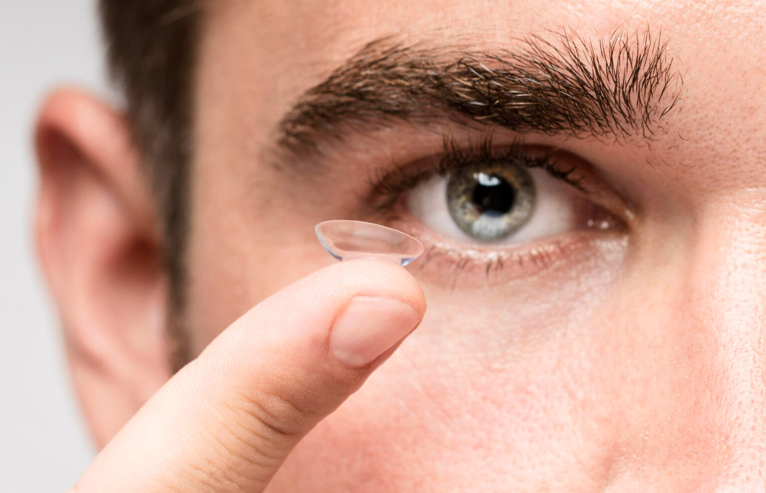Finger hält transparente Kontaktlinse bereit.